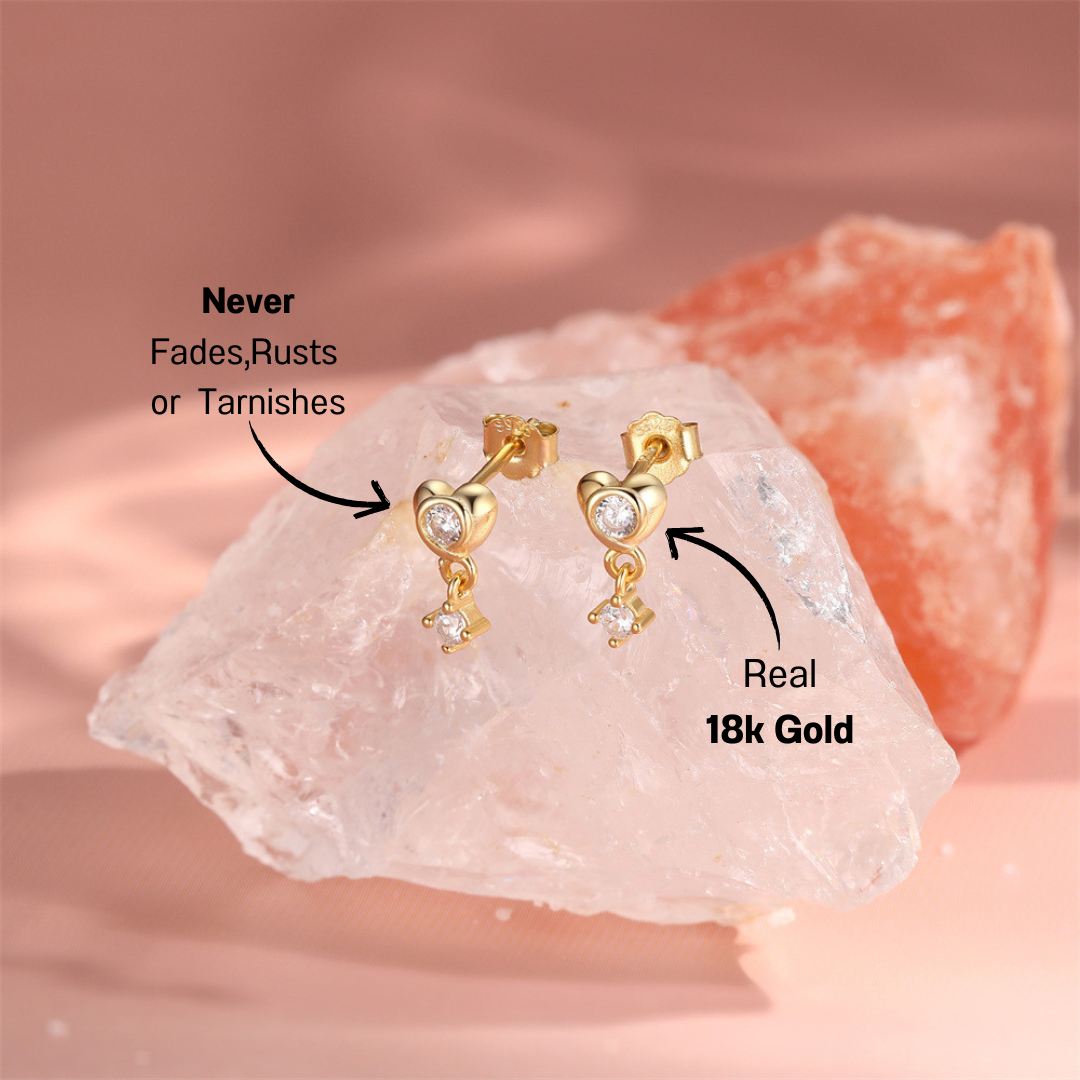 gold-crystal-dangle-earrings-pink-background.png – Charming 14k gold earrings with heart and crystal details, displayed on a soft pink background for a feminine and luxurious aesthetic.