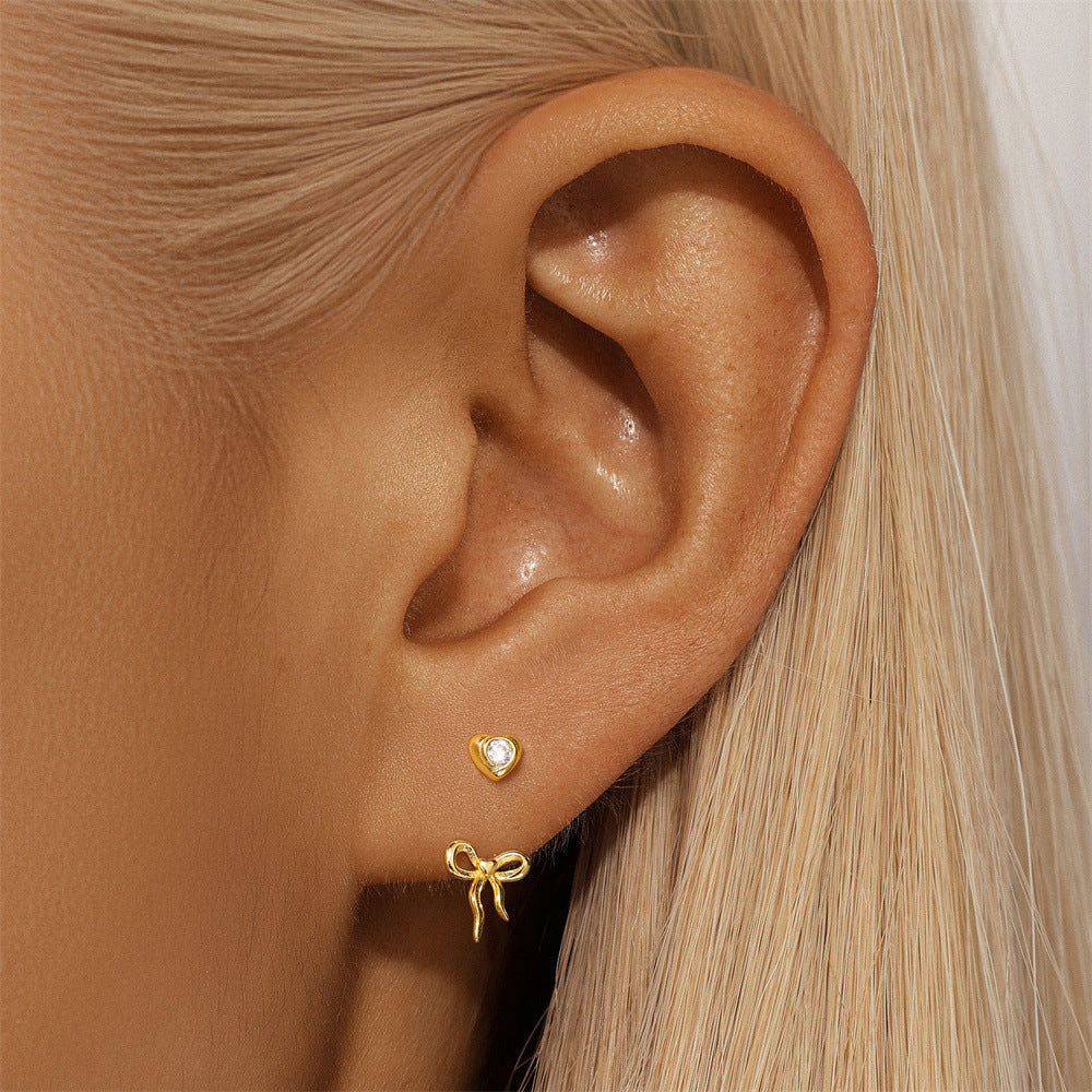 gold-heart-bow-dangle-earrings-on-ear.png – Stylish 14k gold earrings featuring heart studs and bow dangles, shown on a model to highlight their chic and feminine appeal.