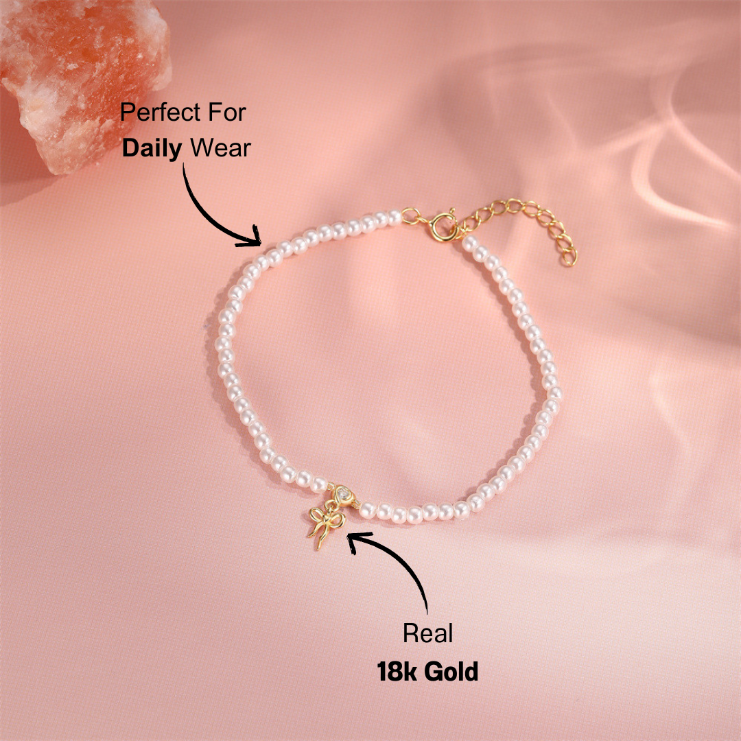 gold-pearl-bracelet-pink-background.png – Stunning pearl bracelet adorned with a 14k gold bow charm, displayed on a soft pink background for an elegant and chic aesthetic.