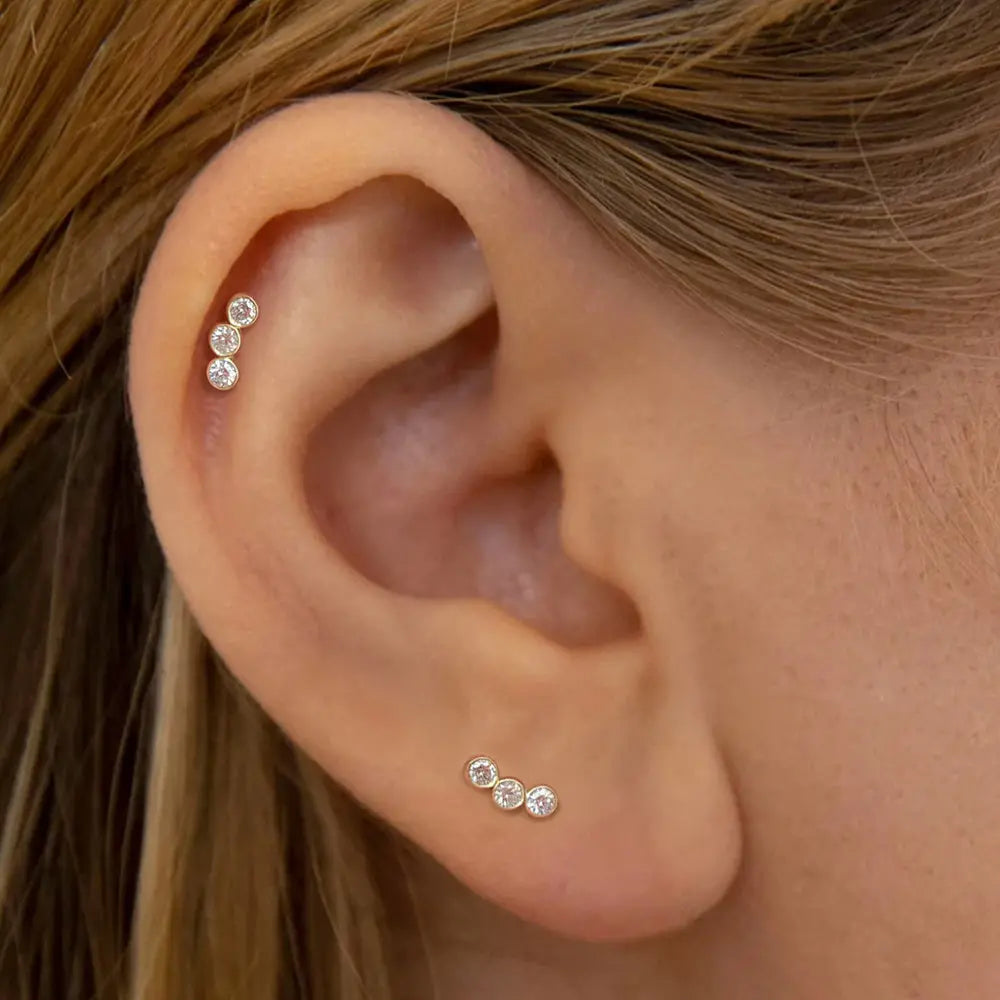 Model wearing a pair of 14k gold-plated 925 sterling silver stud earrings with three zirconia stones, highlighting a chic and minimalistic ear stack.