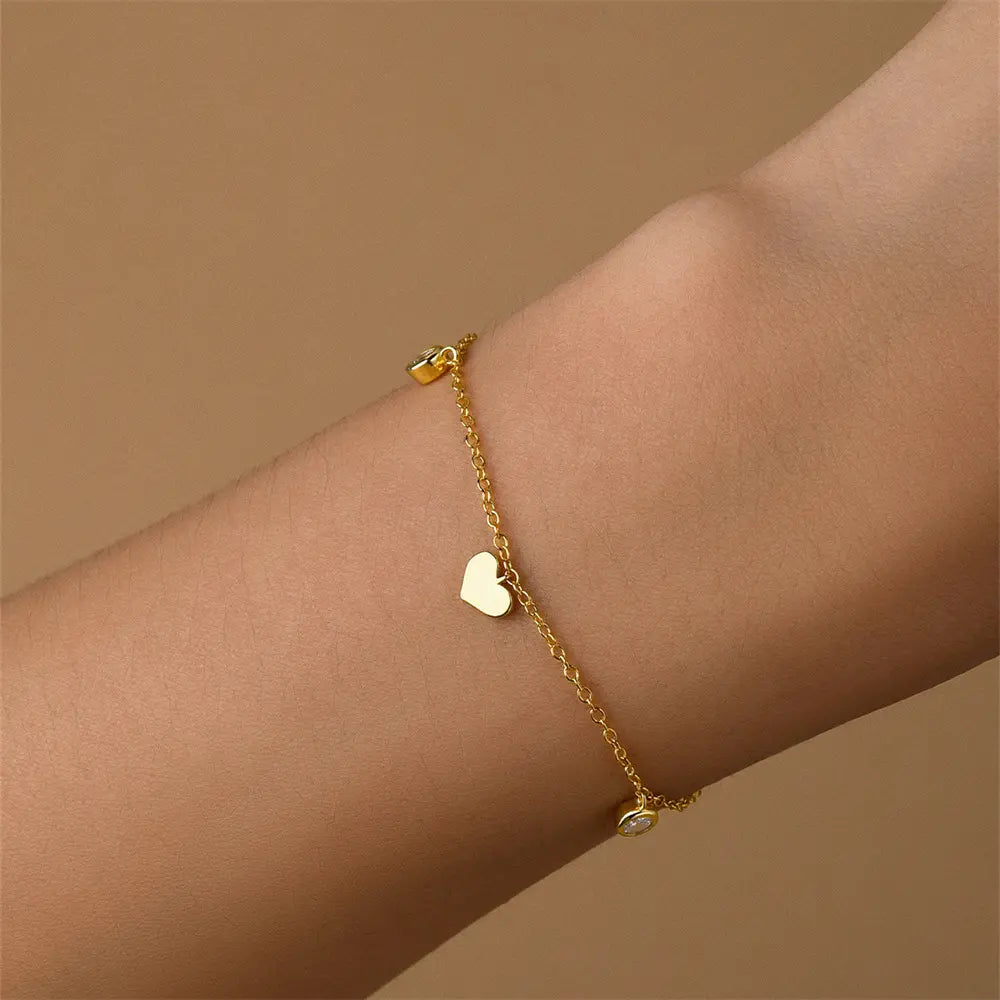 Model showcasing 925 sterling silver heart bracelet with zirconia on gold chain, worn on wrist.