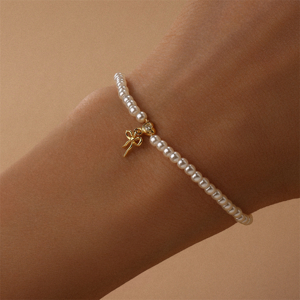 pearl-bracelet-gold-bow-on-wrist.png – Dainty pearl bracelet with a 14k gold bow charm, styled on a wrist to showcase its timeless and sophisticated design.